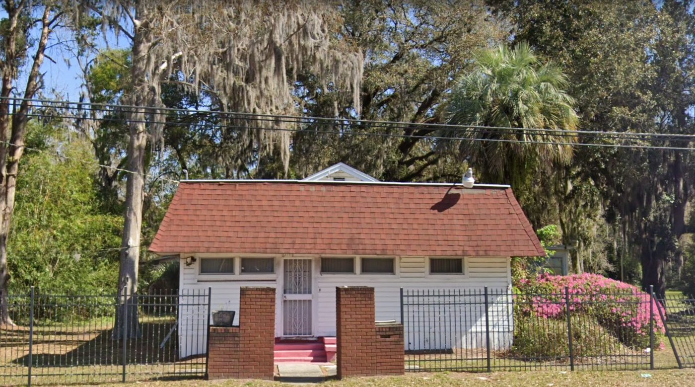 A small white chapter house with a red roof behind an iron fence